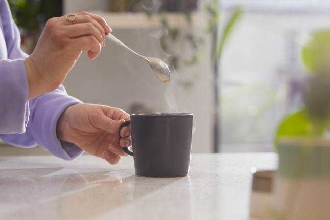 Close up of hands holding spoon after stirring a hot drink in a mug