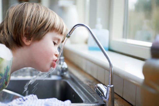 young boy drinking water from tap