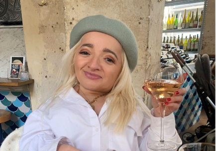 Samantha smiles while holding a glass of rosé wine