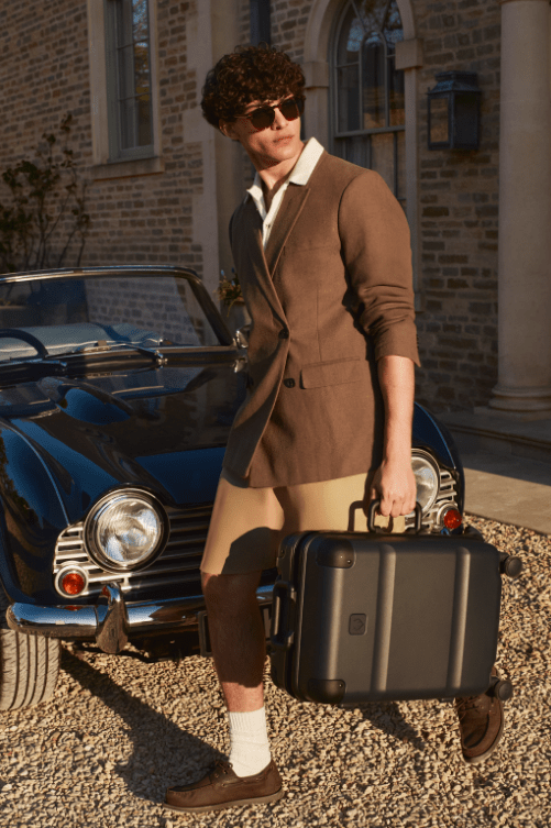 Male holding black suitcase on its side infront of a vintage car