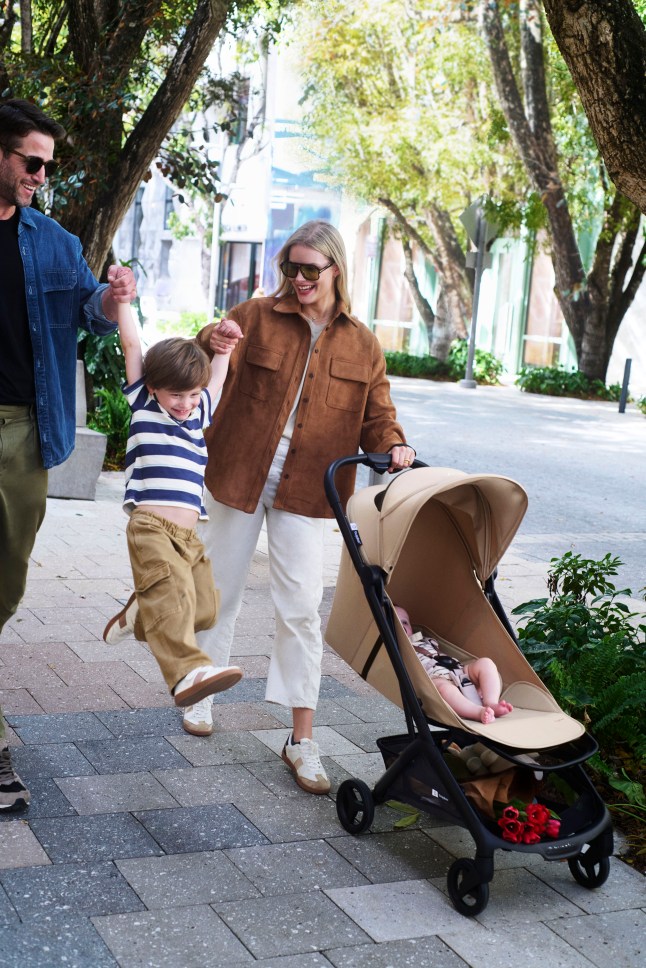 Female and male swinging child in the air whilst pushing a baby in a pram