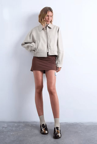 Female wears lightly coloured crop TOPSHOP jacket with dark coloured skirt
