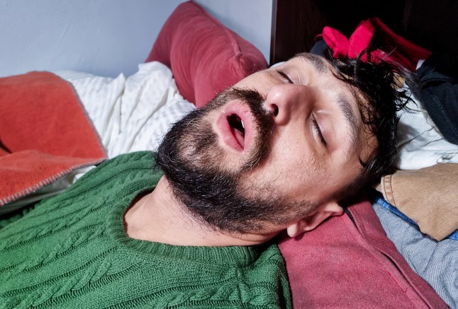 Man asleep in bed snoring, with his mouth open