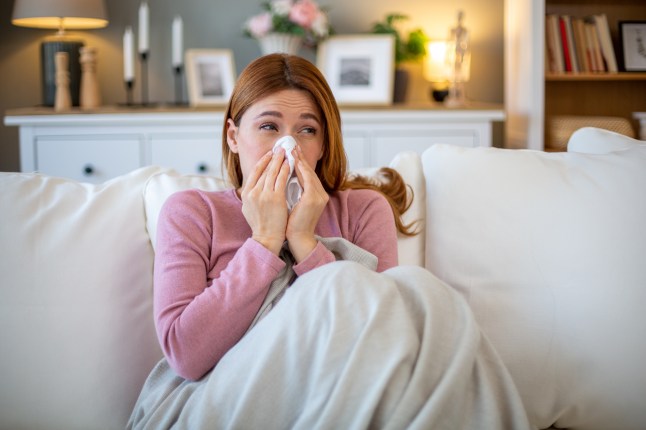 Sick woman blowing nose while sitting on sofa at home