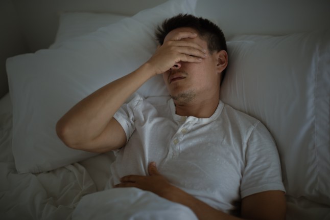 Sleepless man lying in bed feeling tired exhausted stressed waking up unmotivated.