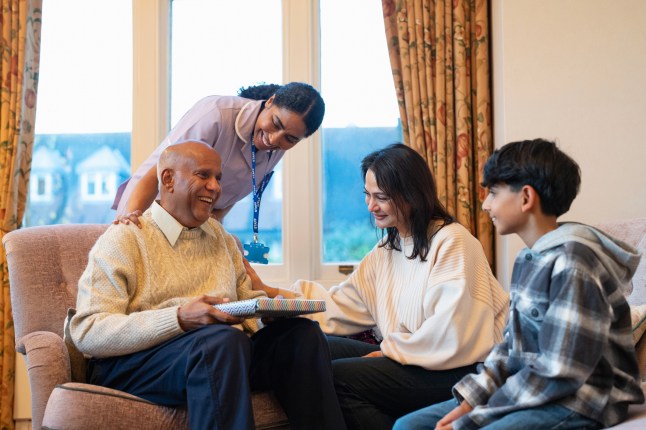 Adult daughter, grandson (12-13) and care giver looking at smiling senior man during visiting in nursing home