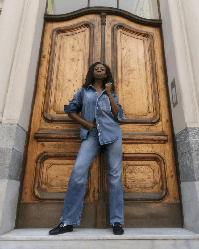 Female stands infront of large wooden door, wearing all denim
