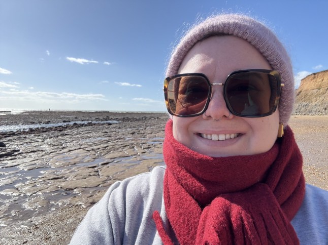 Emma Flint smiles outside, wearing a red scarf and dark glasses