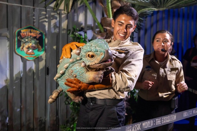 Male holds baby dinosaur, during visit to Jurassic World: The Experience