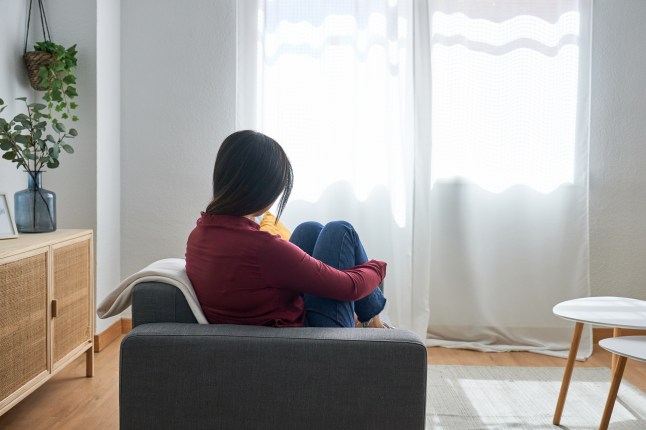 woman sitting on the sofa at home looking at the window with a sad attitude.