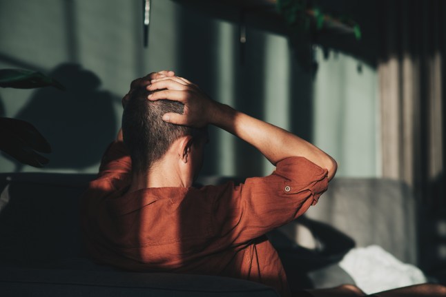 Unpleasant pain. Sad unhappy handsome man sitting on the sofa and holding his forehead while having headache