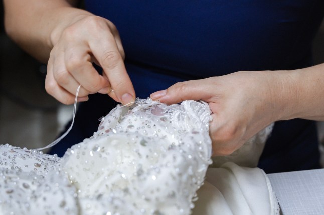 A seamstress's hand sewing beads on a wedding dress