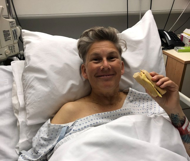 Kit laying in a hospital bed holding a sandwich