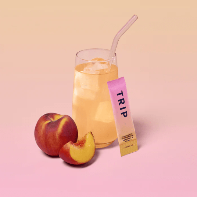 Glass with peach coloured liquids and fruit next to it