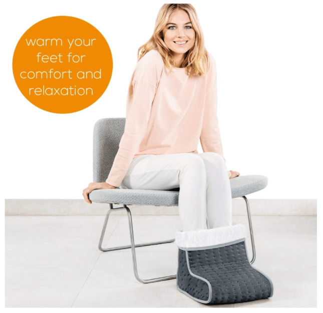 Female sits on a chair, using a heated foot warmer