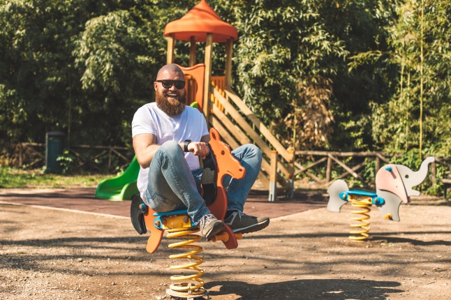 Playful man (dad) riding wooden rocking horse in a park