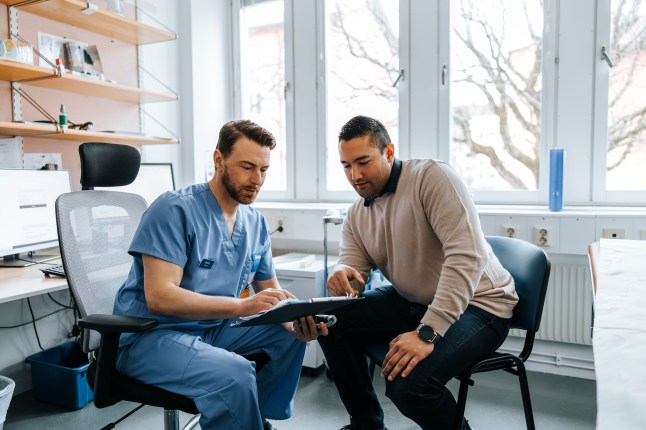 Male medical expert discussing reports with male patient during visit at hospital