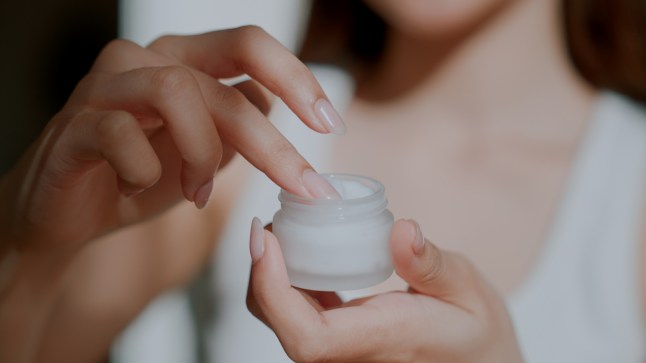 Young woman opening beauty product jar and scooping up a portion for use.