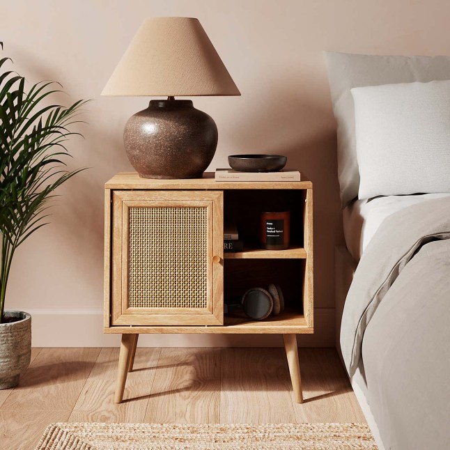 Rattan bedroom side table with brown lamp on top, next to bed