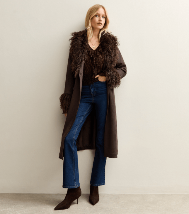 Model wears dark brown coat with faux fur