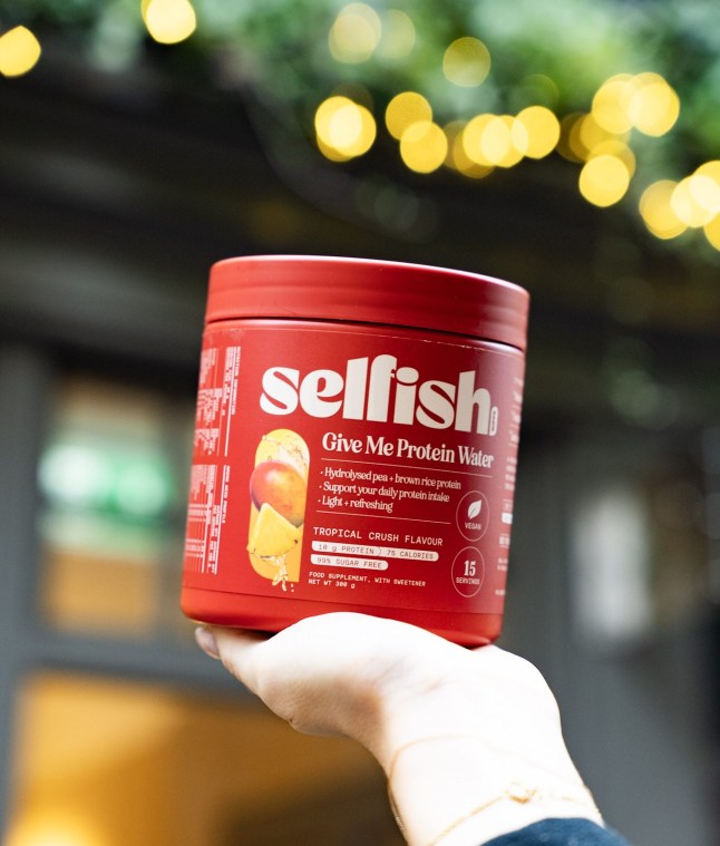 A hand holding the Selfish Supps Give Me Protein Water 300g Tropical Crush Flavour