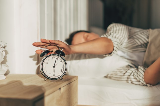 Hand of woman turning off alarm clock on night table.