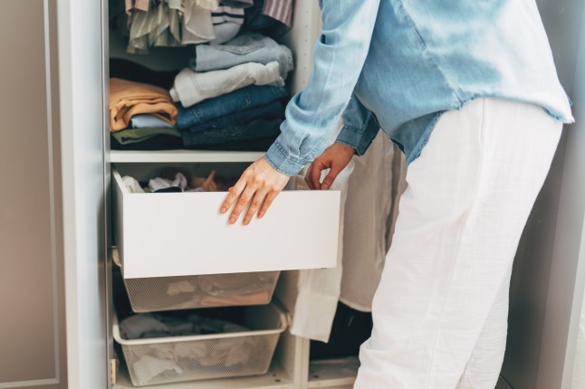 Happy young redhead woman putting clothes and underwear in storage container during wardrobe cleaning. Smiling female neatly puts clothing into cupboard modern storage system comfortable organization