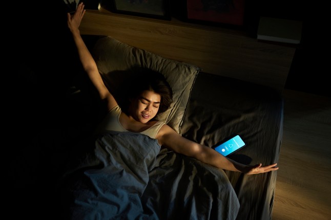 Smiling woman stretching arms and waking up in bed at home