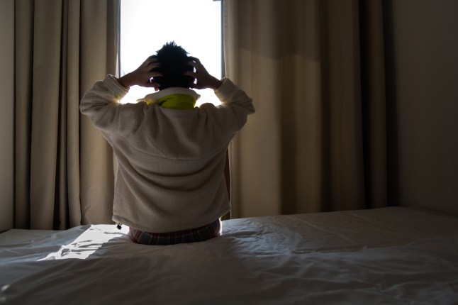 Depressed teenager boy sitting on bed with head in hands
