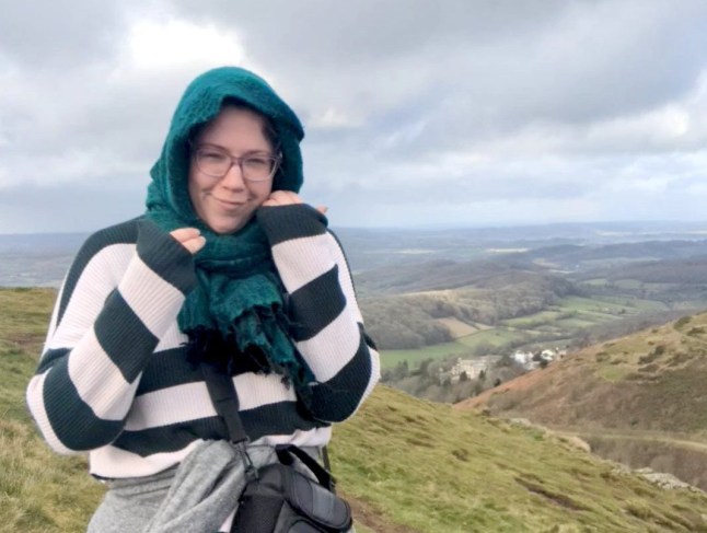 Hannah Shewan Stevens stands in front of rolling hills and a grey sky