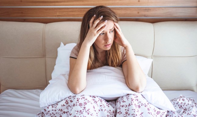 Shot of an attractive young woman sitting on her bed looking unhappy. Sleepy woman feeling hangover headache after waking up in bed, suffering from lack of sleep deprivation, insomnia, morning headache or migraine