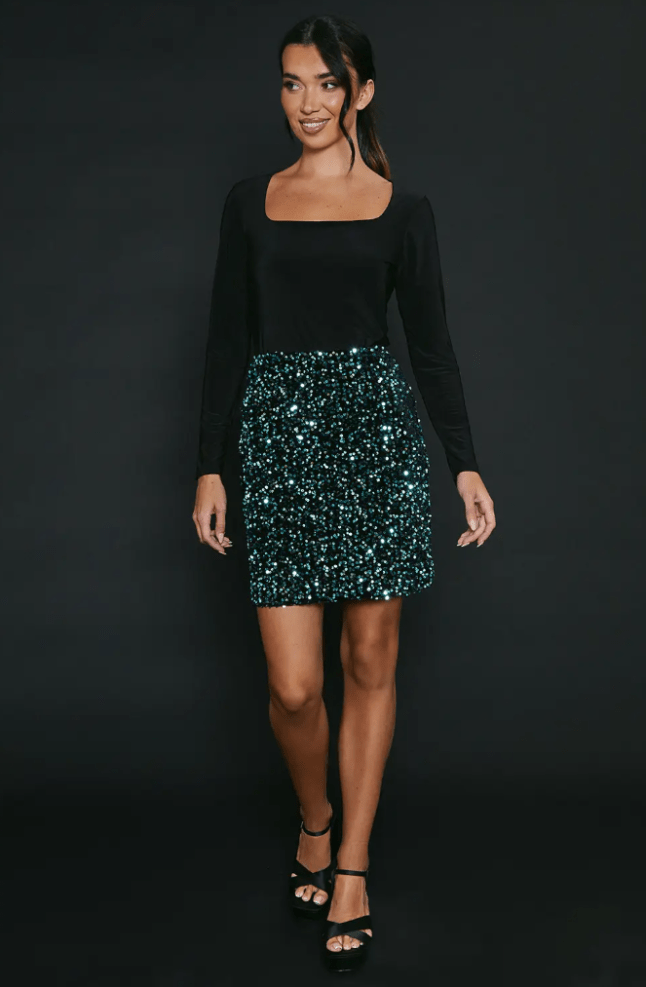 Model wears green sequin skirt with black, long-sleeved top