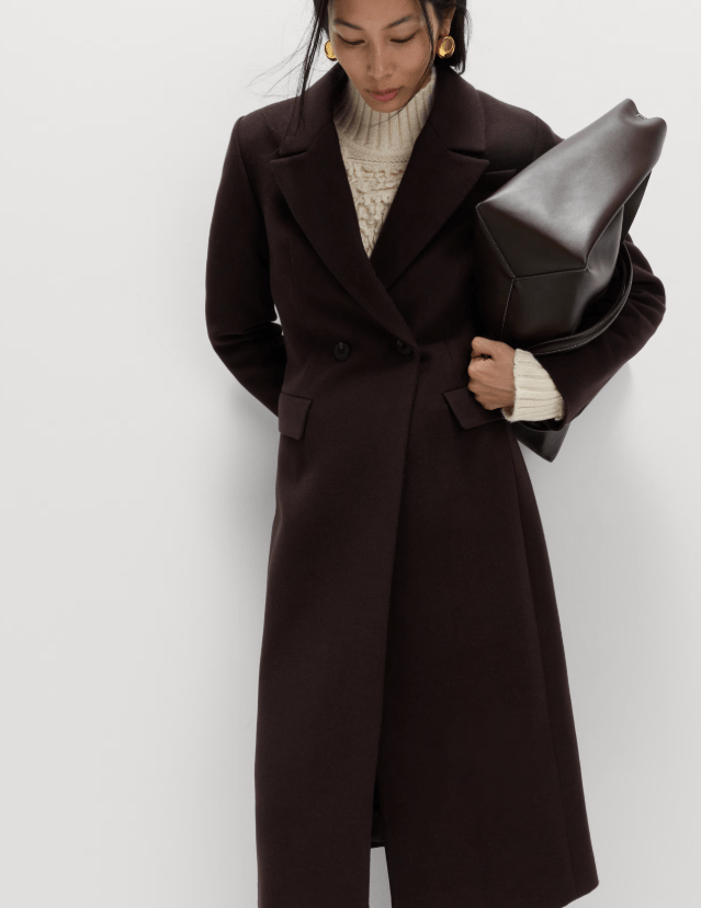 Female wears dark coloured coat with light sweater underneath