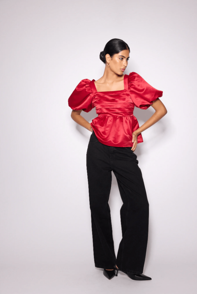 Female wears red satin top with black trousers