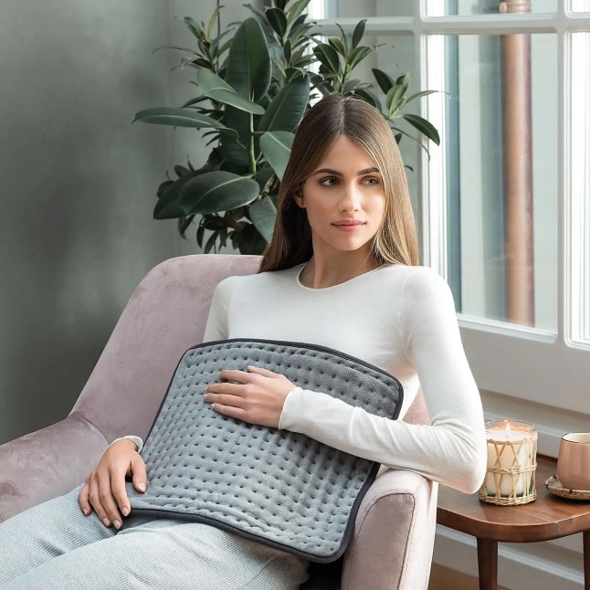 Female holds grey heated pad against her stomach