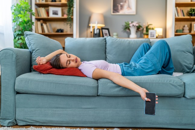 Young woman napping on sofa holding phone