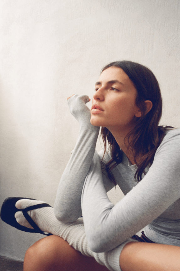 Female rests chin on her hand, wearing long-sleeved grey top