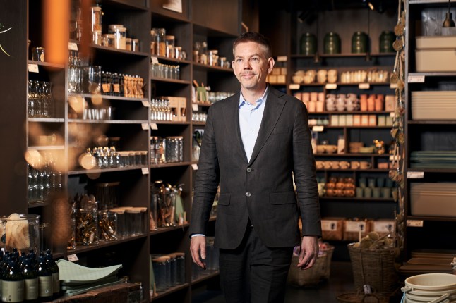 Mikkel Grene, the chief executive of Søstrene Grene, poses inside one of the stores, wearing a suit.