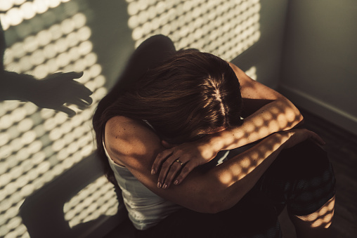 Depressed woman sitting on the bed at home while a shadow hand gives help.