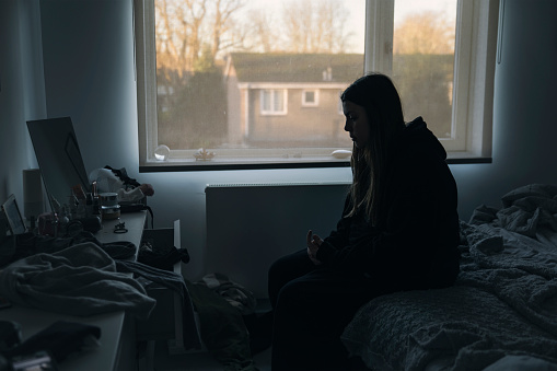 Powerful shot of a young woman sitting on her bed - negative emotion