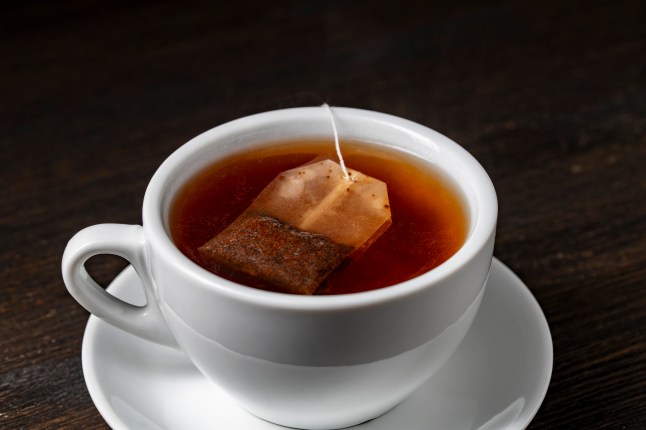 Tea bag in white cup with hot water on wooden table, closeup