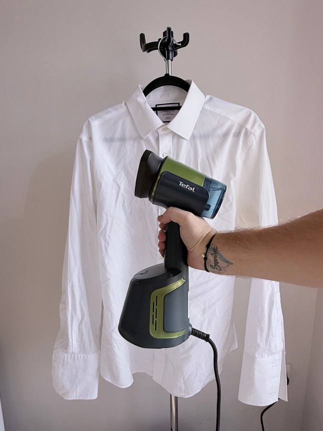 Hand holding steamer, in front of white shirt