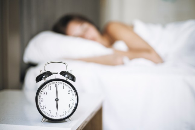 A young woman enjoys a peaceful sleep while an old-fashioned alarm clock ticks nearby in a well-decorated bedroom